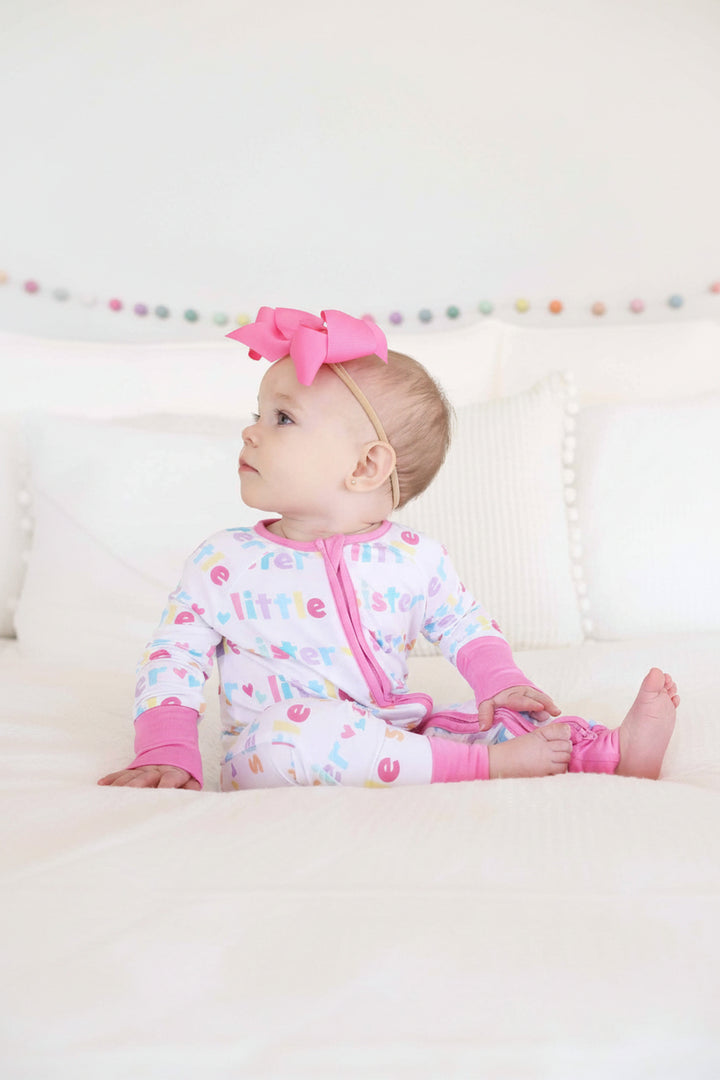 baby girl wearing little sister zip romper and pink bow headband