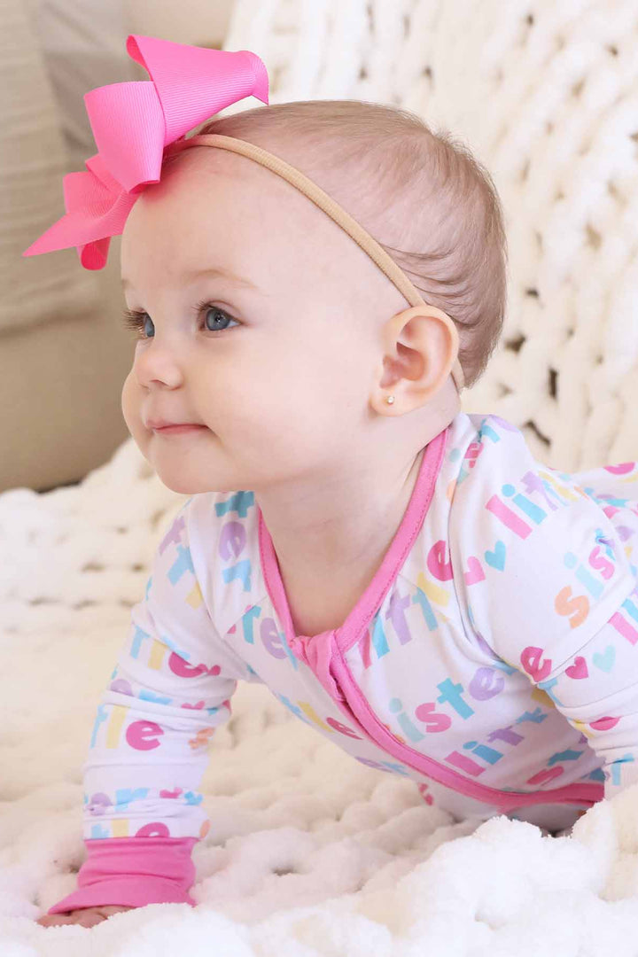 baby girl wearing little sister zip romper and pink bow headband