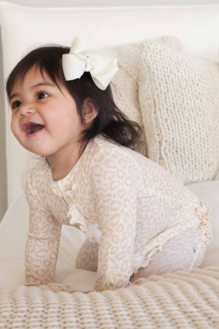 baby girl kneeling and wearing a neutral leopard bamboo viscose footie pajama 