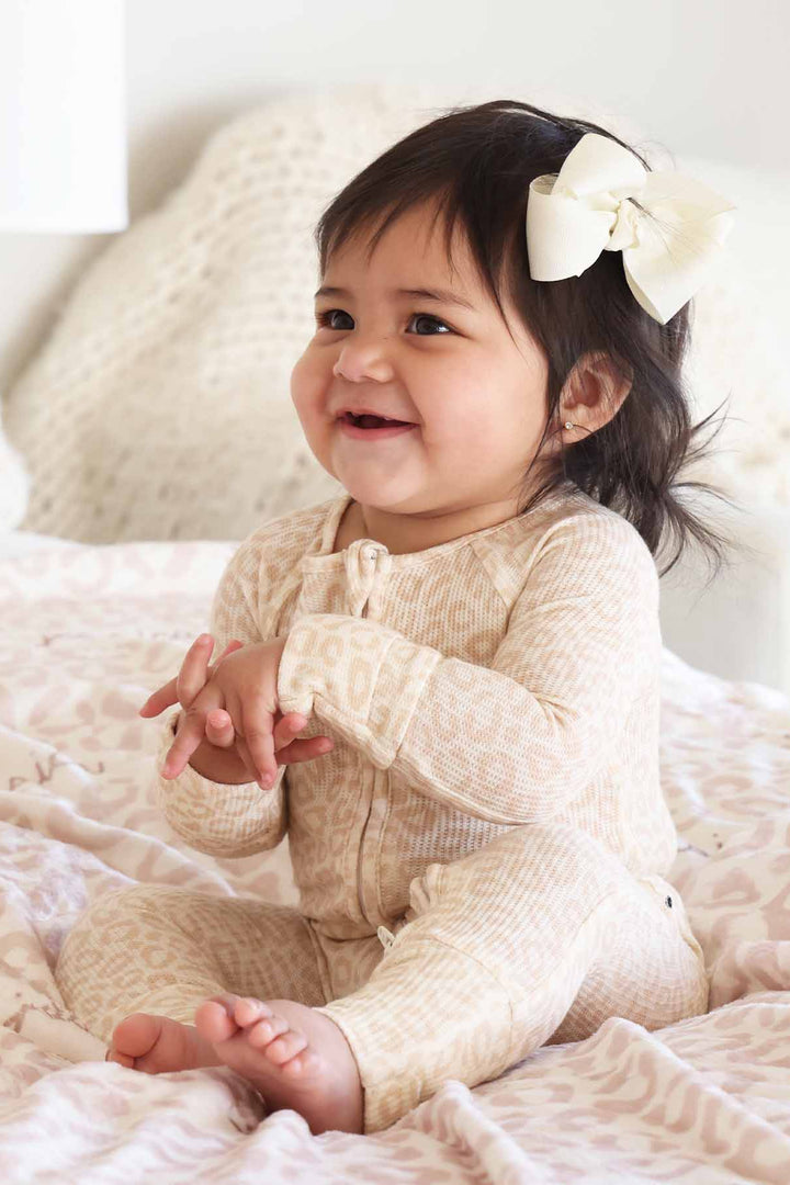 toddler sitting on bed in neutral leopard pajama romper 