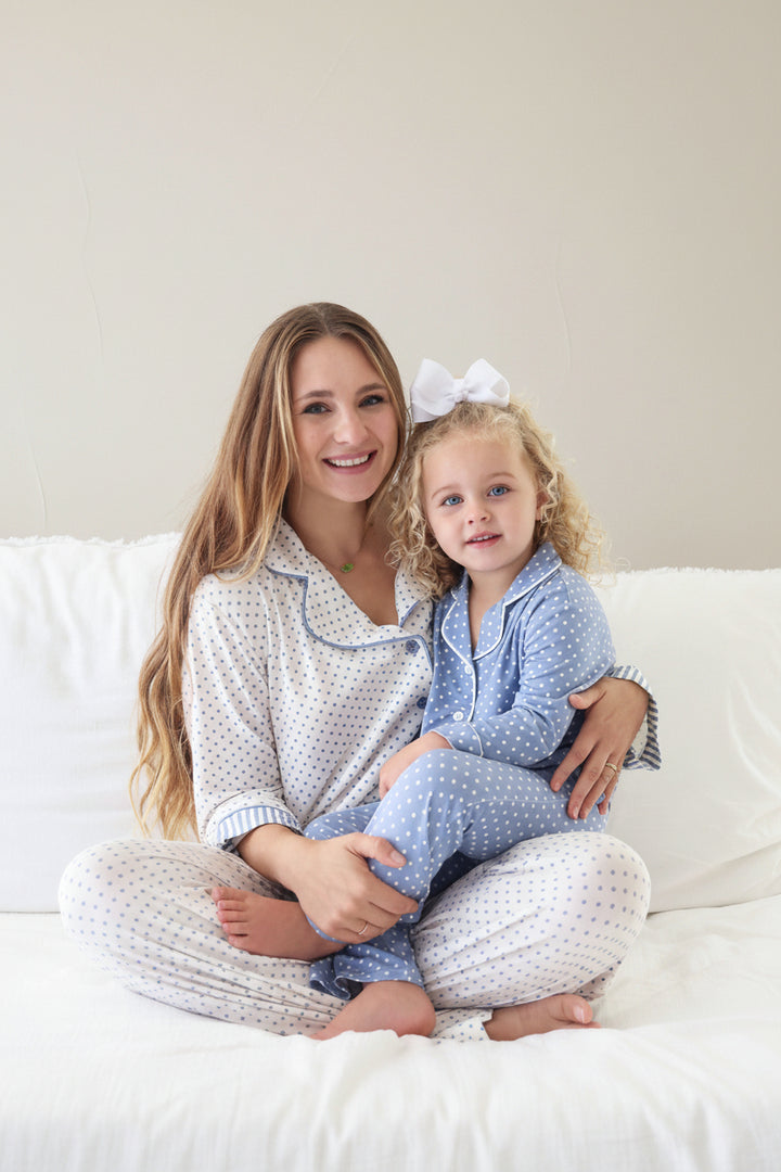 mom sitting criss cross on bed in white long sleeve lounge set with blue polka dots with daughter sitting on her lap in matching lounge set blue with white polka dots 
