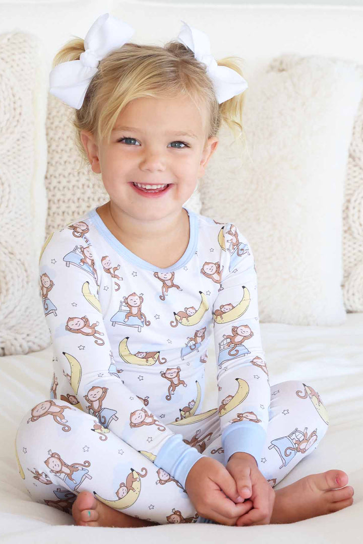 girl sitting on bed wearing monkey and banana pajama set 