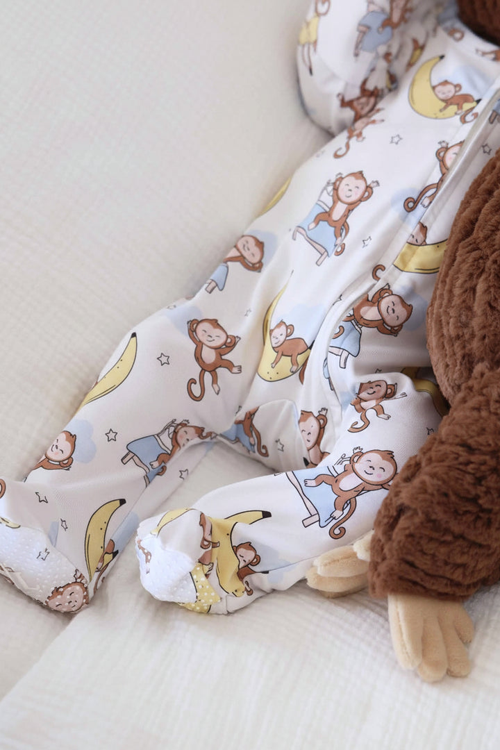 close up of baby laying on bed in money and banana footie next to a monkey stuffed animal 
