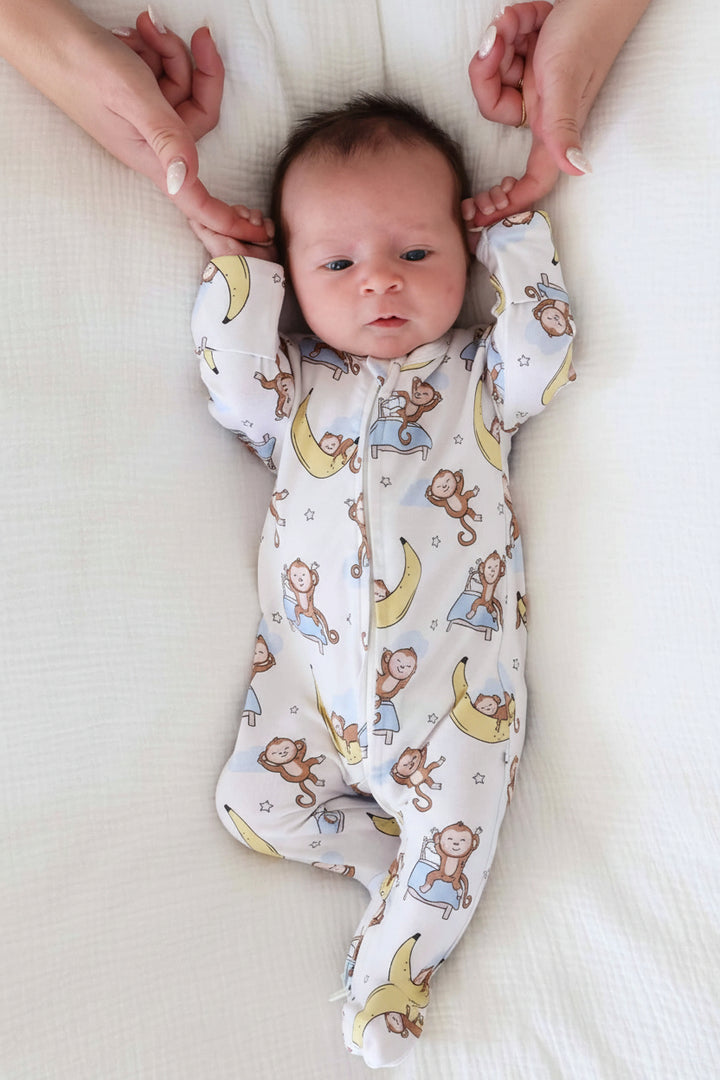 baby laying on bed wearing monkey see, monkey snooze bamboo viscose zipper footie for babies gender neutral