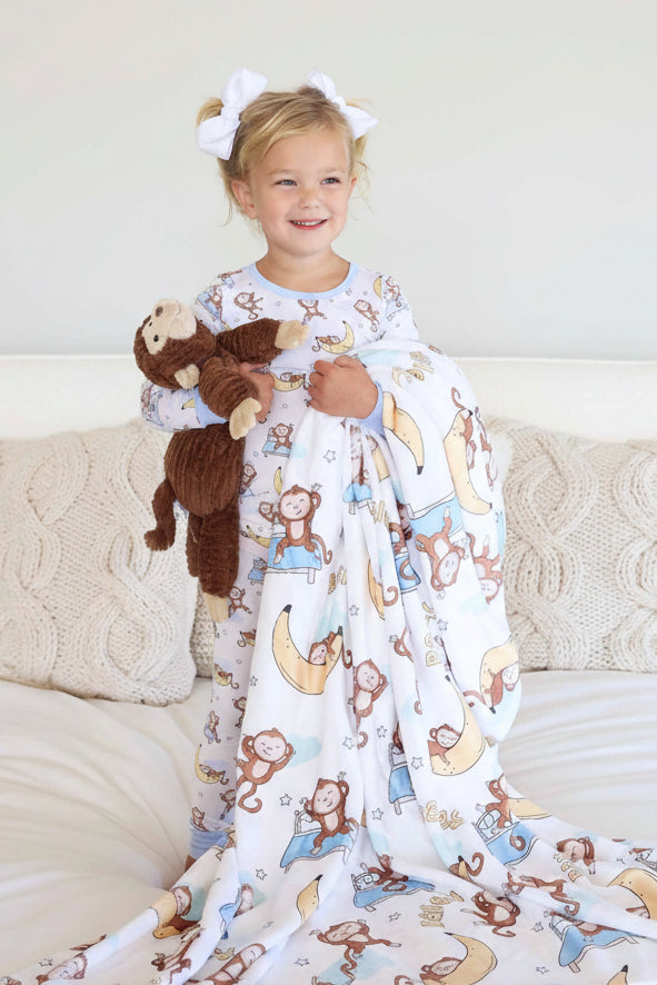 girl holding a monkey and banana personalized kids blanket wearing matching pajamas and holding a monkey stuffed animal standing on a bed