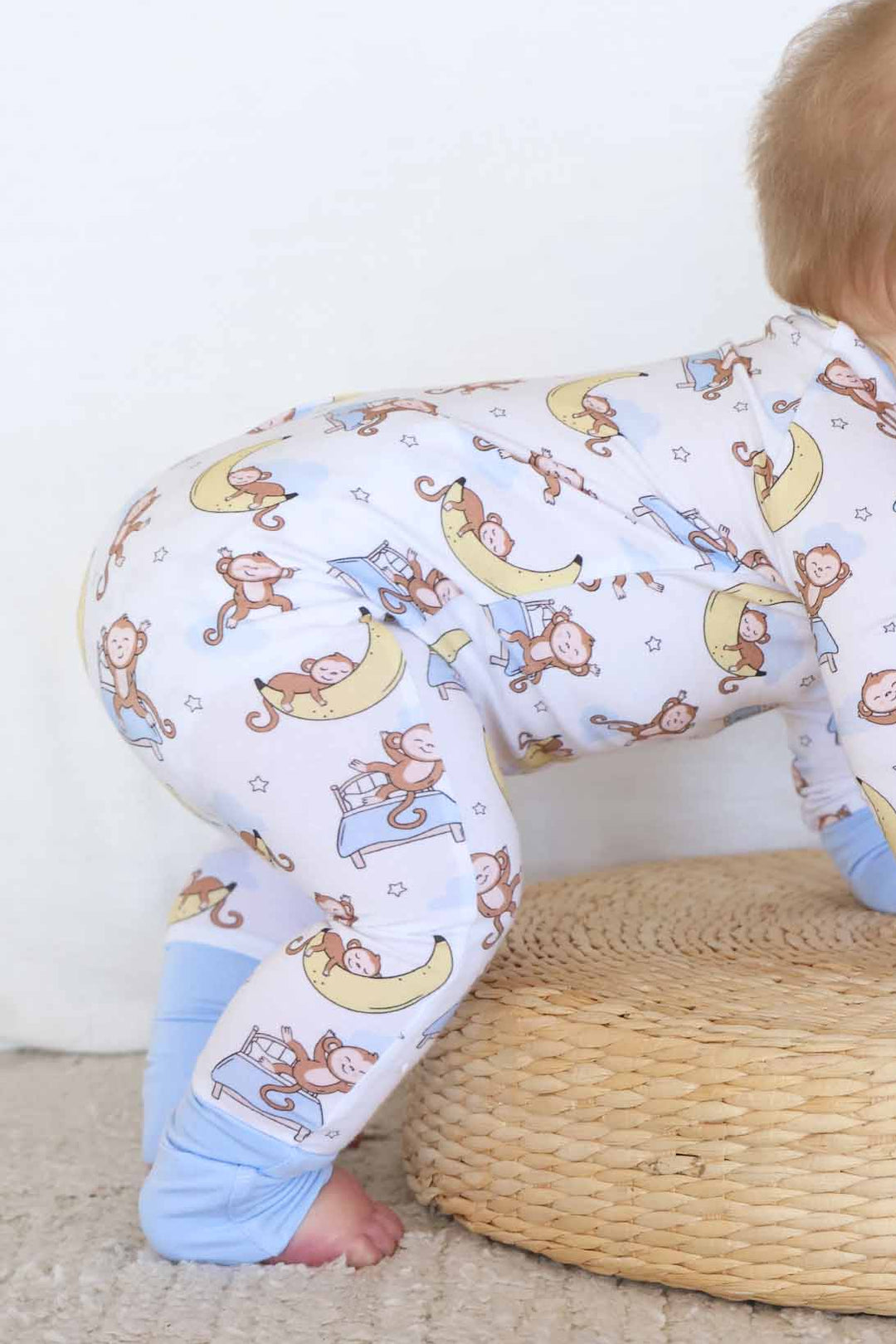 toddler crawling on wooden platform in monkey pajama romper 