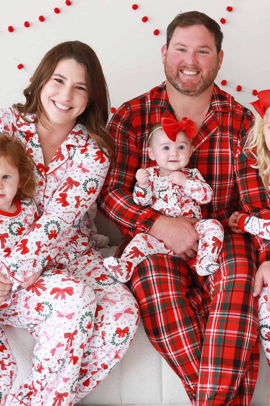 Father in Caden Lane plaid pajama set with Mother and three daughters in Caden Lane wreath and bow matching pajama sets