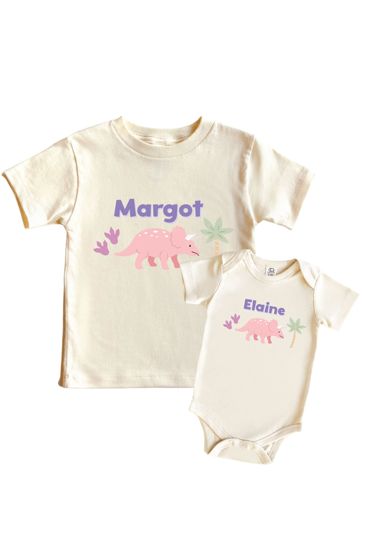 Natural cream kids tee and baby bodysuit set featuring a pink triceratops dinosaur graphic with pastel plant accents and personalized name in purple lettering