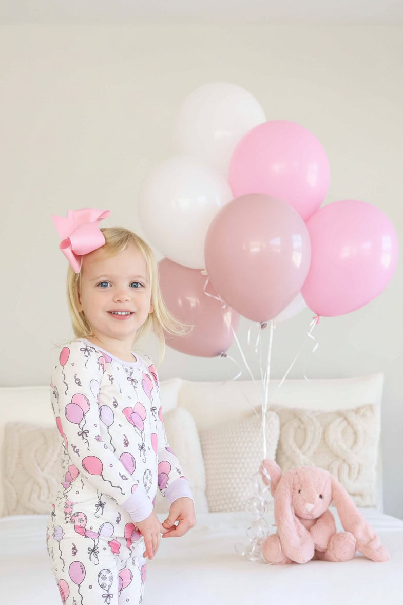 girl wearing a pink balloon two piece pajama set with a pink bunny in the background holding balloons 