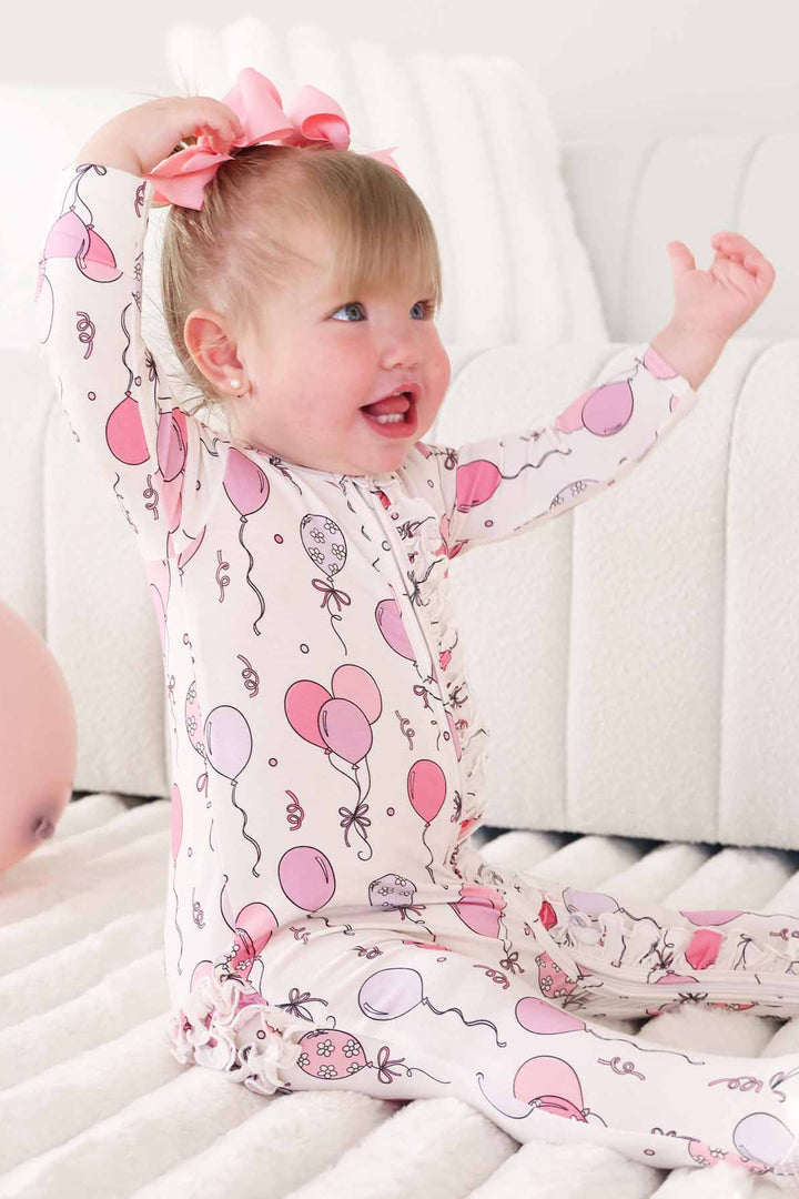 baby girl wearing a pink and purple balloon and streamer footie pajama 