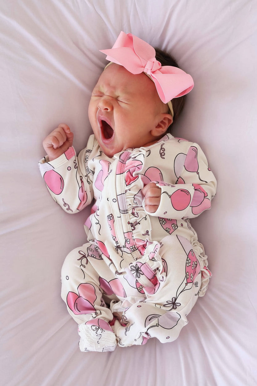yawning baby wearing a pink balloon ruffle zipper footie with matching solid pink ribbon bow headband 