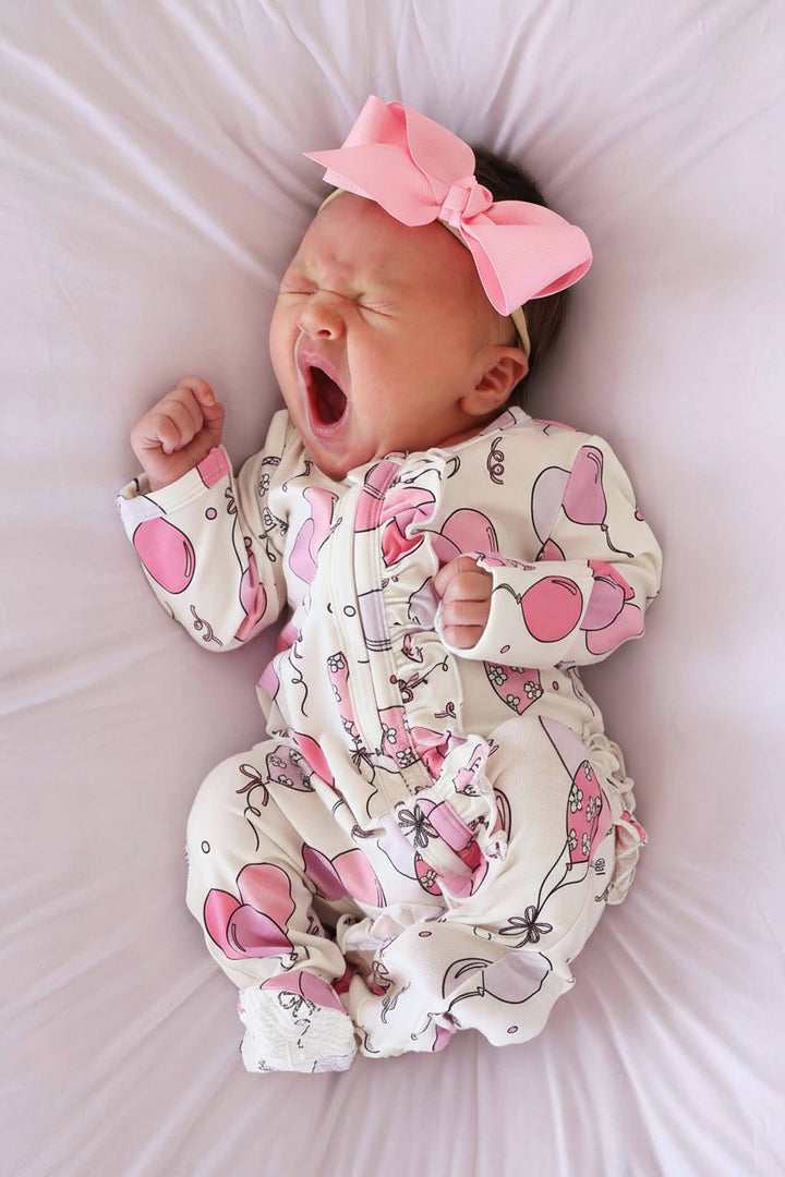 yawning baby wearing a pink balloon ruffle zipper footie with matching solid pink ribbon bow headband 