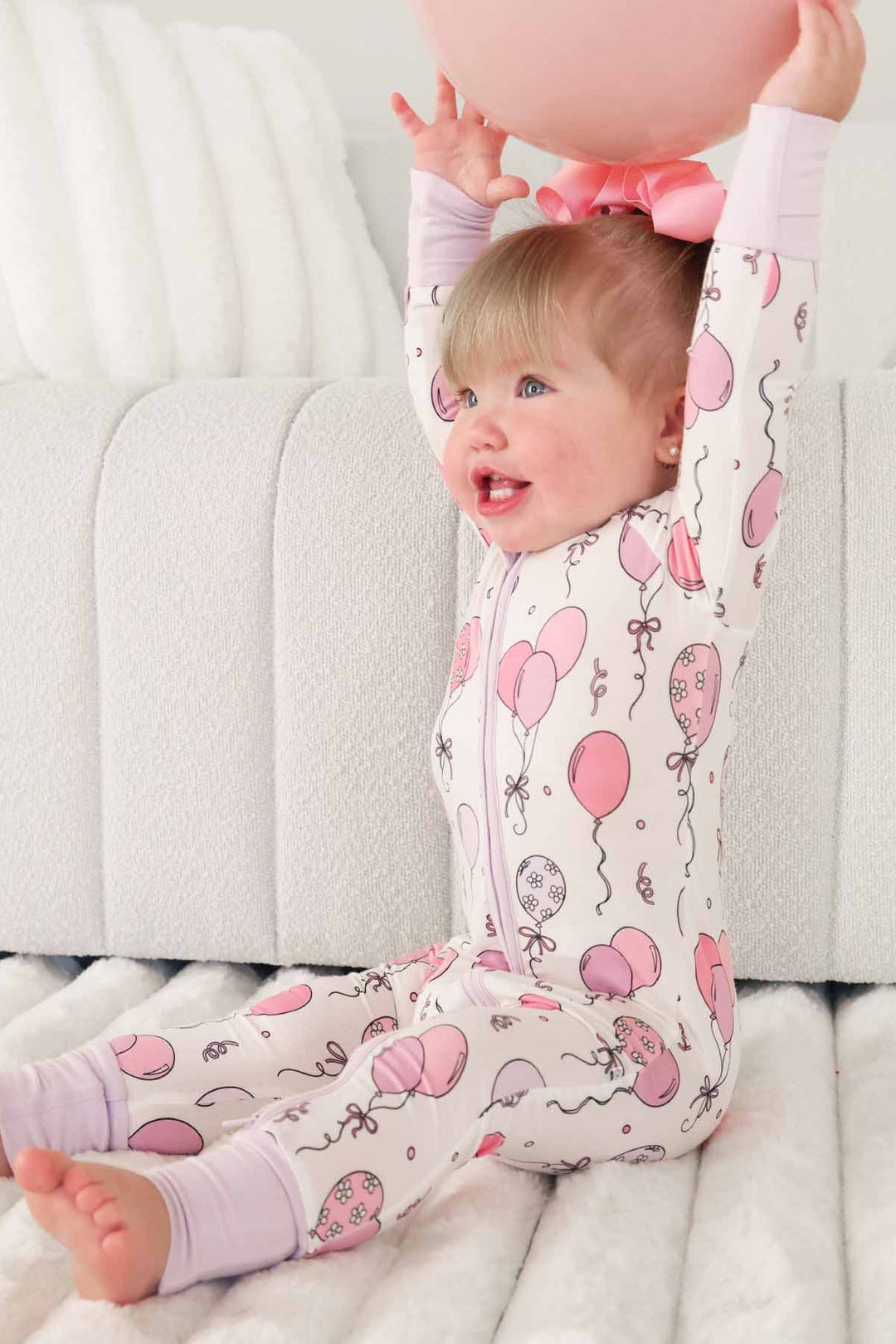 girl wearing pink and purple balloon zip romper pajama holding a balloon above her head 