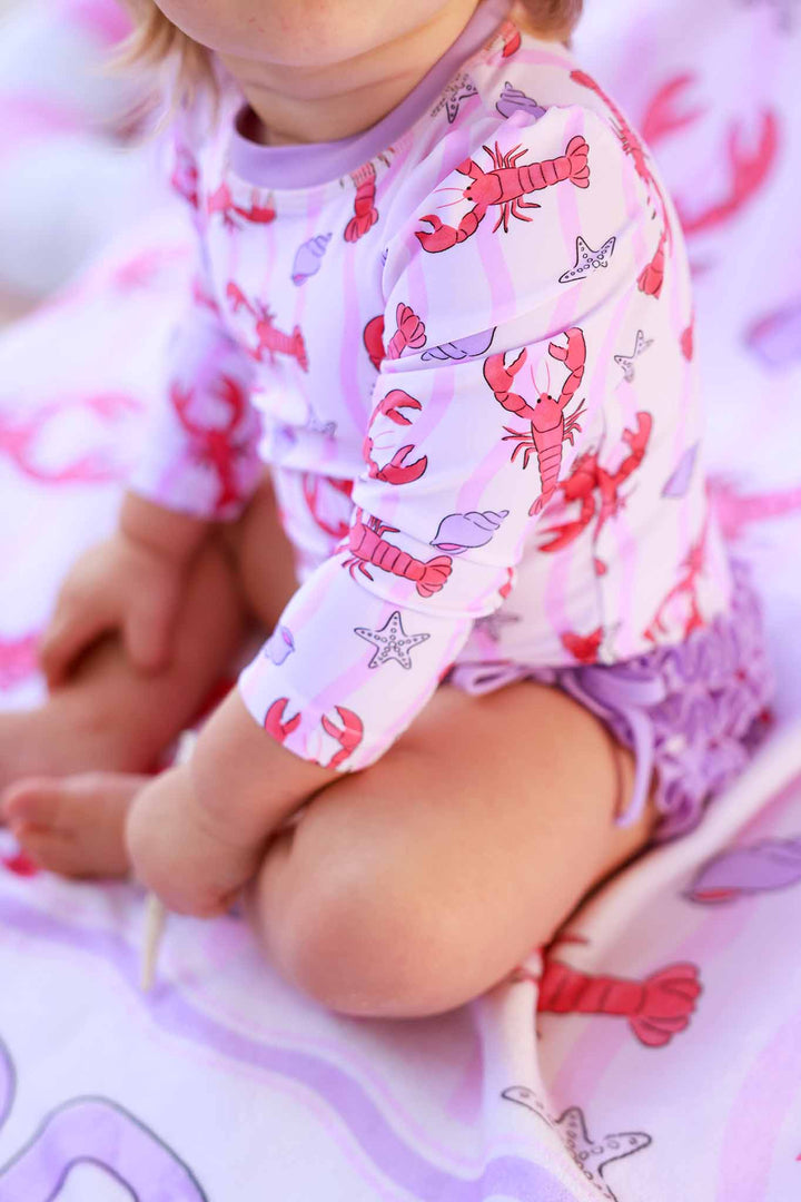 closeup of pinch me pink long sleeve rash guard swimsuit with purple ruffles on the bottom 