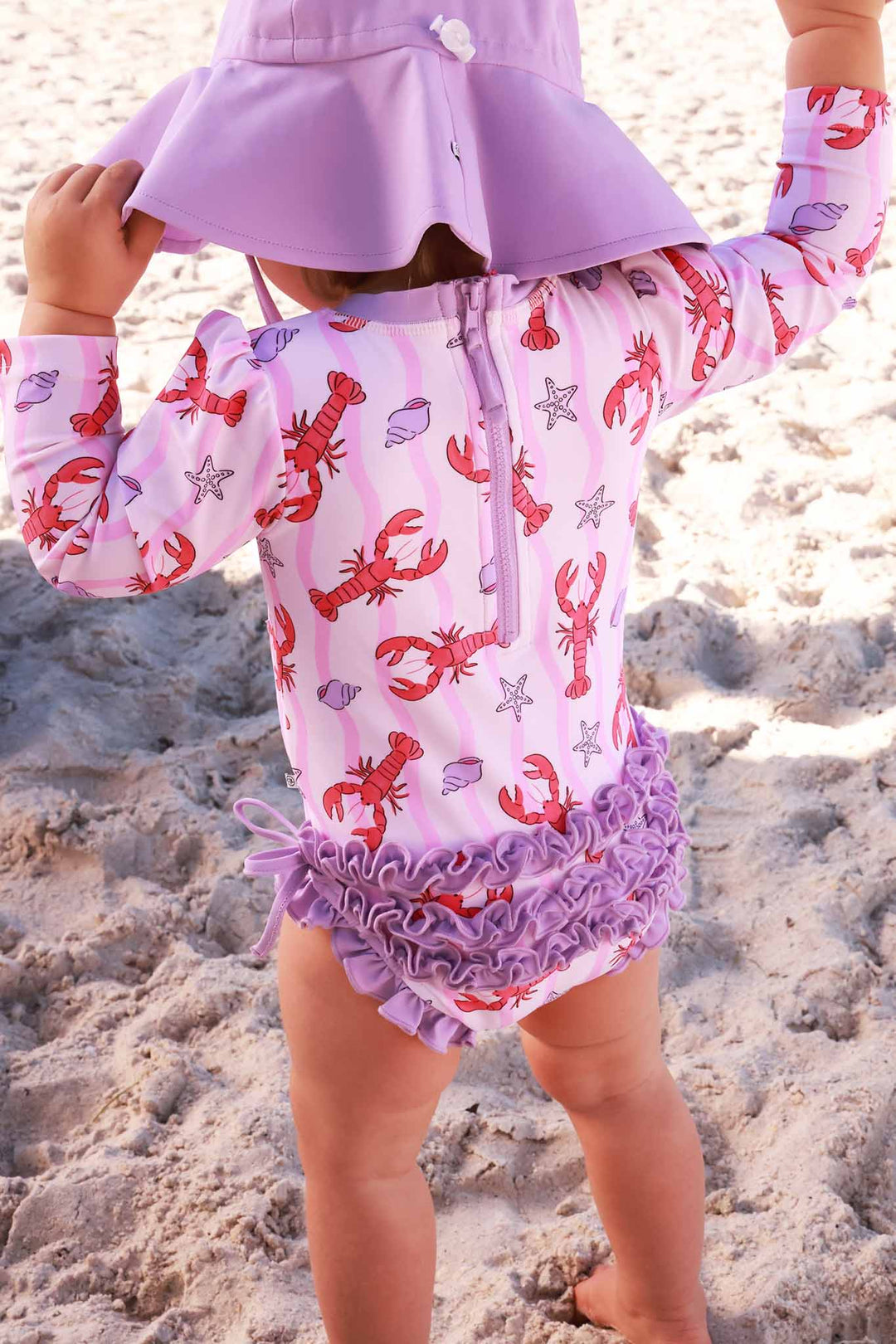 back view of pinch me long sleeve rash guard with ruffle bottom with matching light purple sun hat 