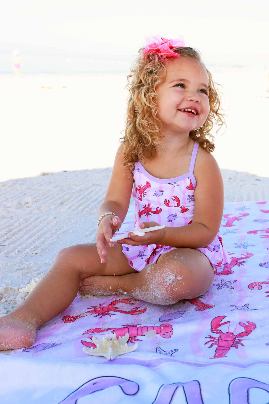 girl sitting on lobster personalized beach towel for girls wearing a matching tankini swimsuit 