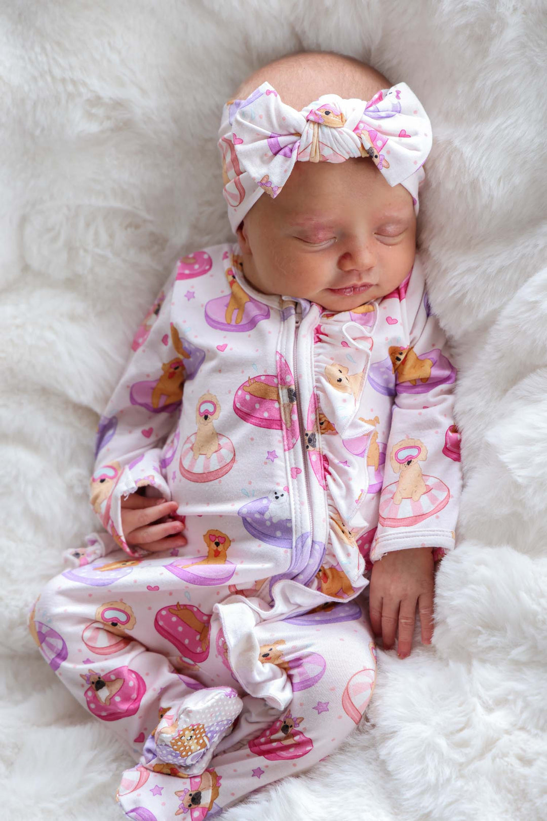 baby girl laying on white blanket in poolside pups pink ruffle zipper footie with matching headwrap