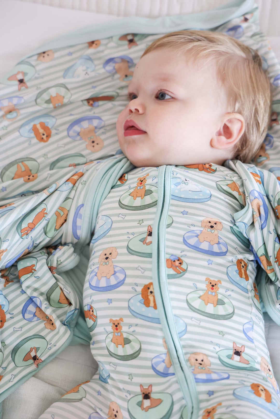 baby boy laying down in poolside pups pajama romper with bamboo blanket over the shoulders