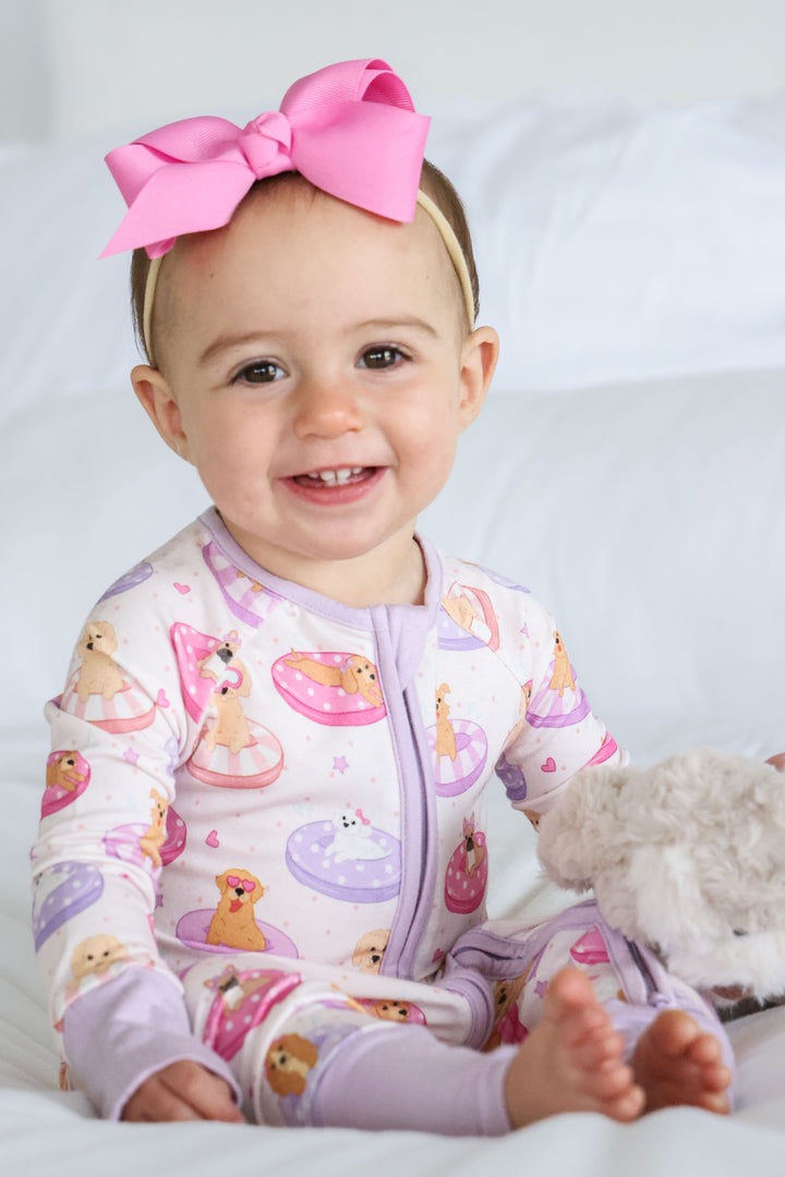 smiling girl in poolside pups convertible zip romper in pink with a matching ribbon bow headband 