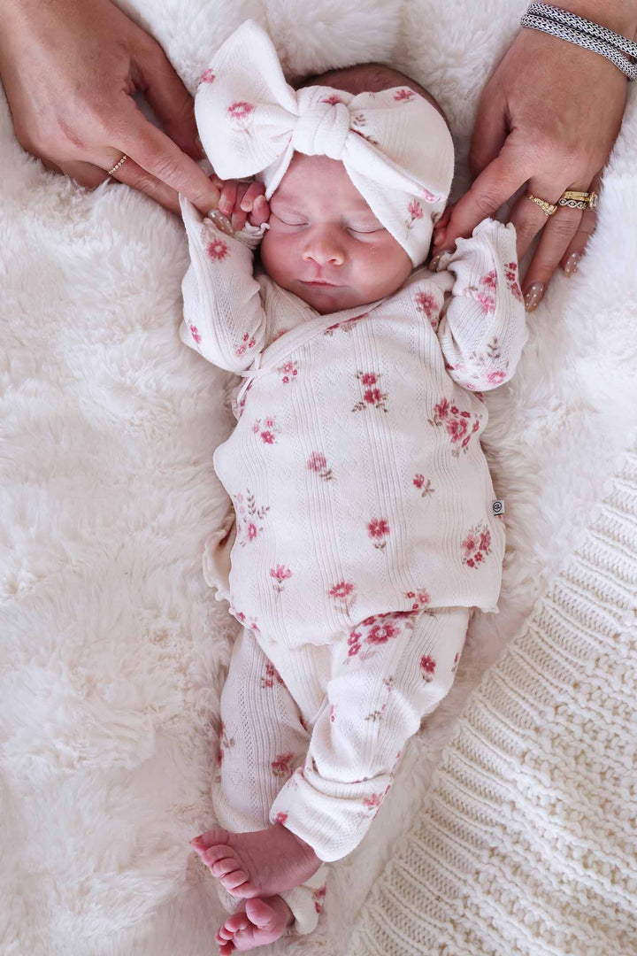 baby girl laying down holding mom's fingers in precious posies pointelle crossover set with matching headwrap 