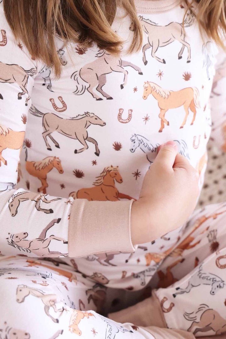 girl wearing printed two piece kids pajamas with ponies, horses, and horseshoes print - caden lane