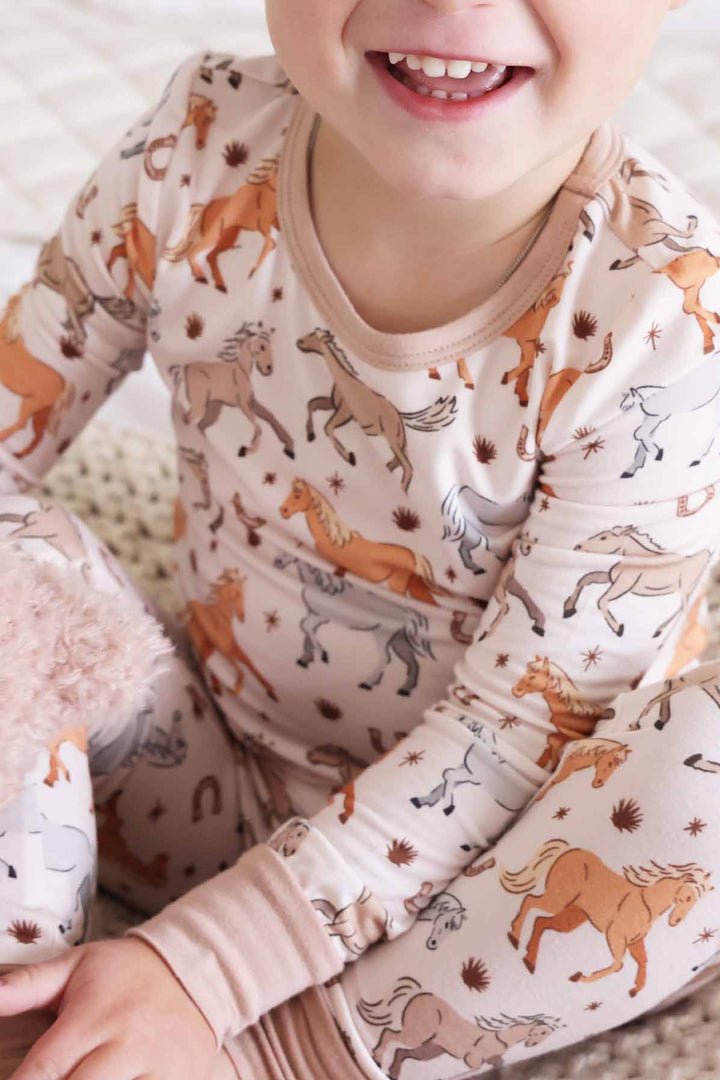 boy wearing printed two piece kids pajamas with ponies, horses, and horseshoes print - caden lane