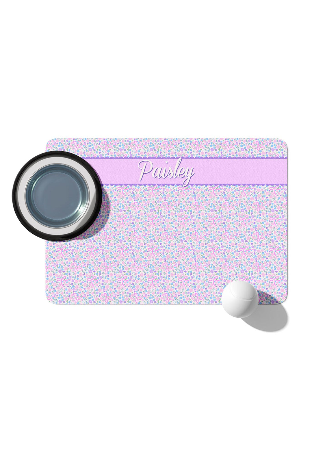 Personalized pet placemat in the Ribbon Garden print with a lavender stripe personalized with the name "Paisley", shown with a pet bowl and ball in a product mock-up
