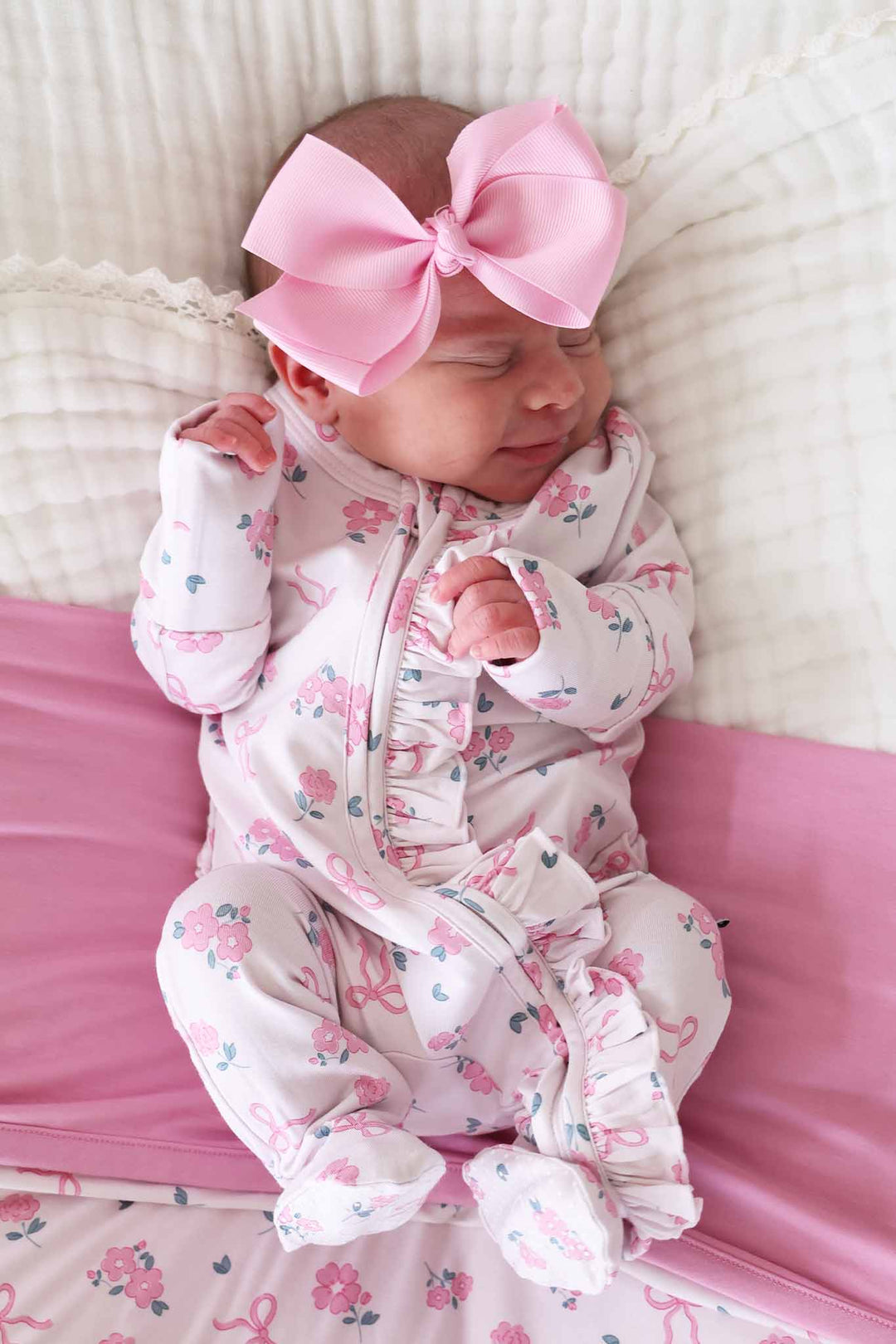 smiling baby girl laying on ribbon and roses pink double sided bamboo blanket and wearing a matching ruffle zipper and solid pink ribbon bow headband 