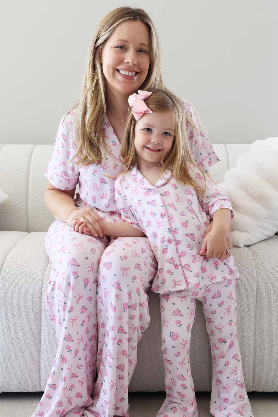 mom sitting on couch with daughter leaning against her in matching ribbon and roses pink collared button up lounge sets 