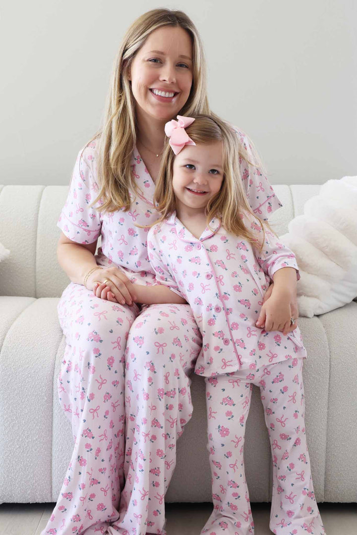 mom sitting on couch with daughter leaning against her in matching ribbon and roses pink collared button up lounge sets 
