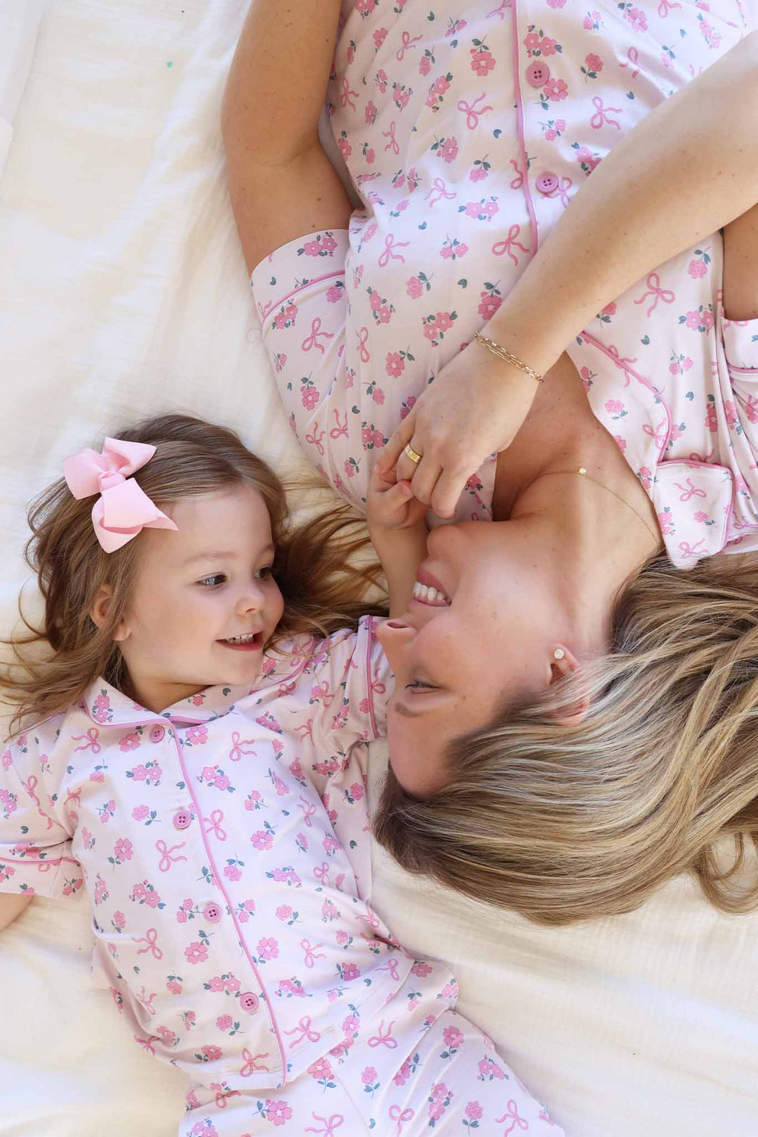 mom and daughter laying down looking at each other wearing matching flare pant button up lounge sets in ribbon and roses pink print 