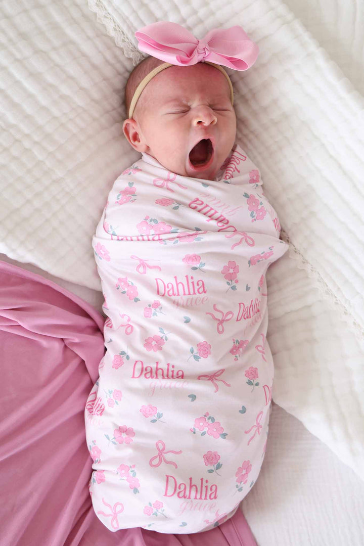yawning baby girl wrapped in pink flower and ribbon bow personalized swaddle blanket 