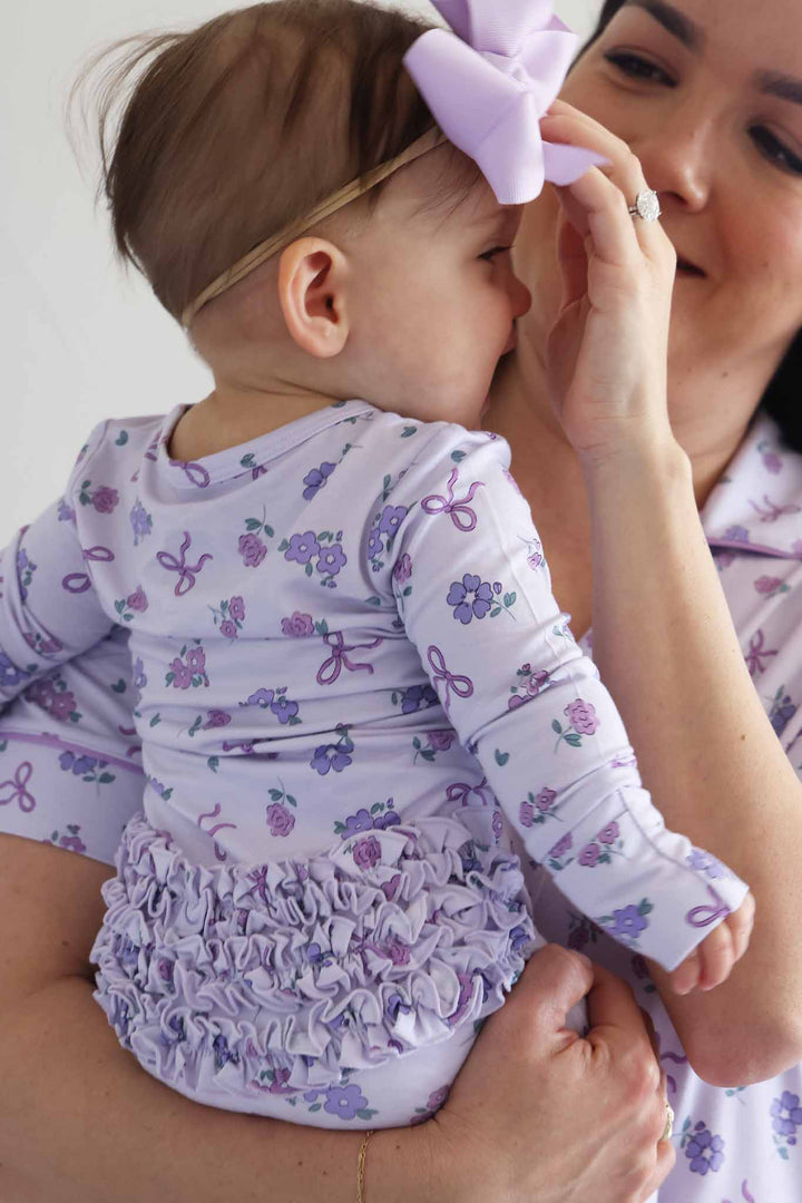 mom holding baby girl in ribbon and roses ruffle bottom zipper footie and lilac ribbon bow headband 