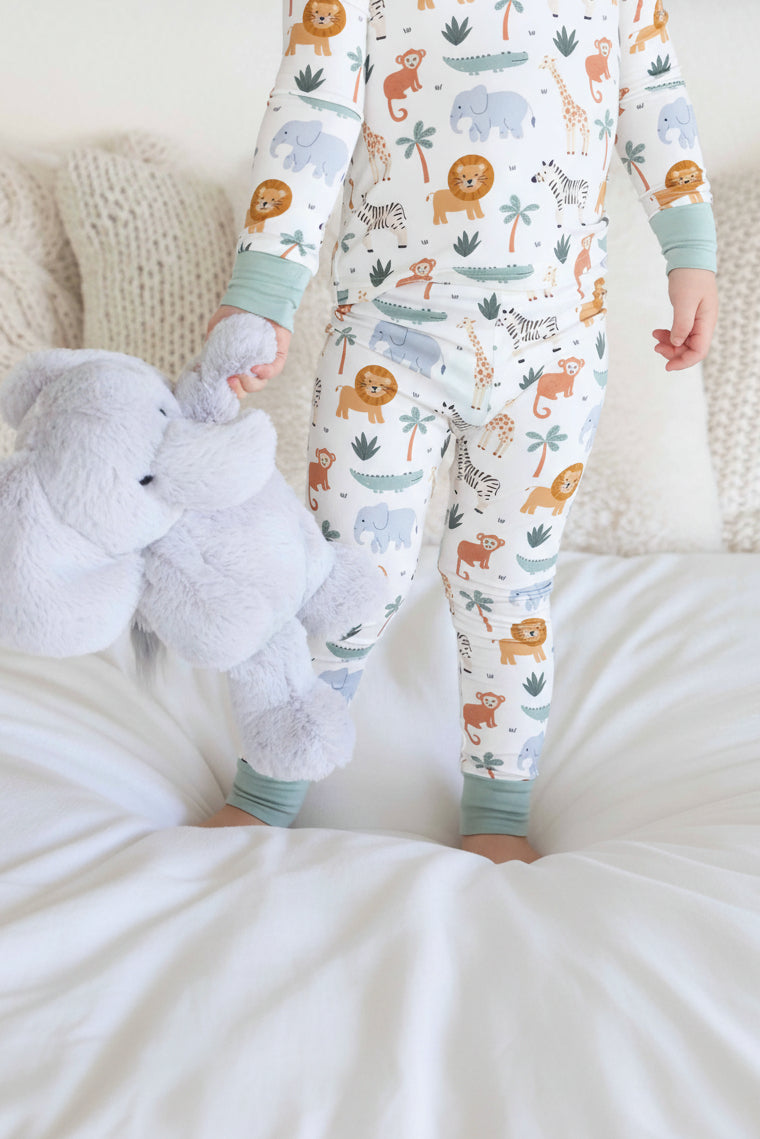 kid wearing safari animal two piece pajama set holding an elephant stuffed animal 