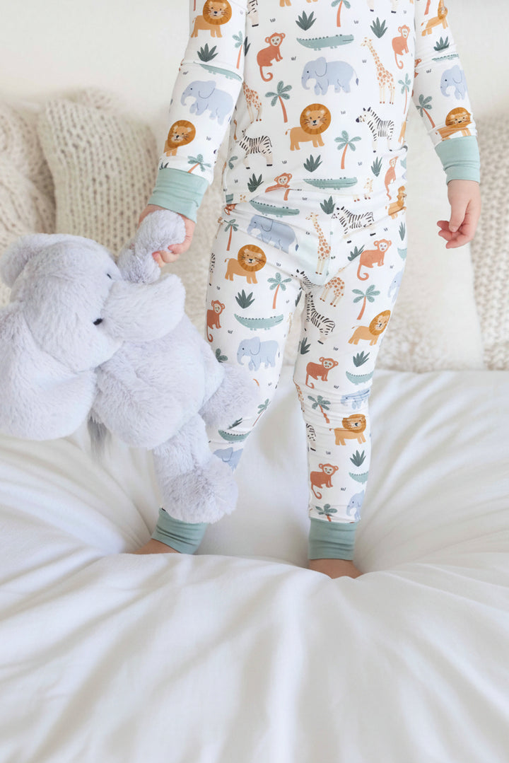 kid wearing safari animal two piece pajama set holding an elephant stuffed animal 