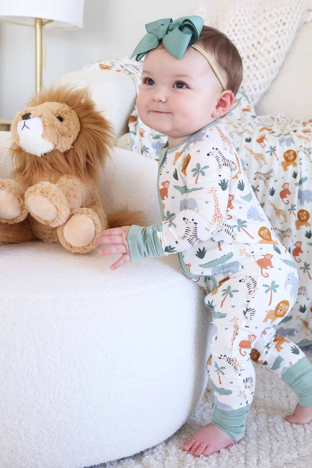 standing toddler girl wearing safari animal pajama romper with lion stuffed animal