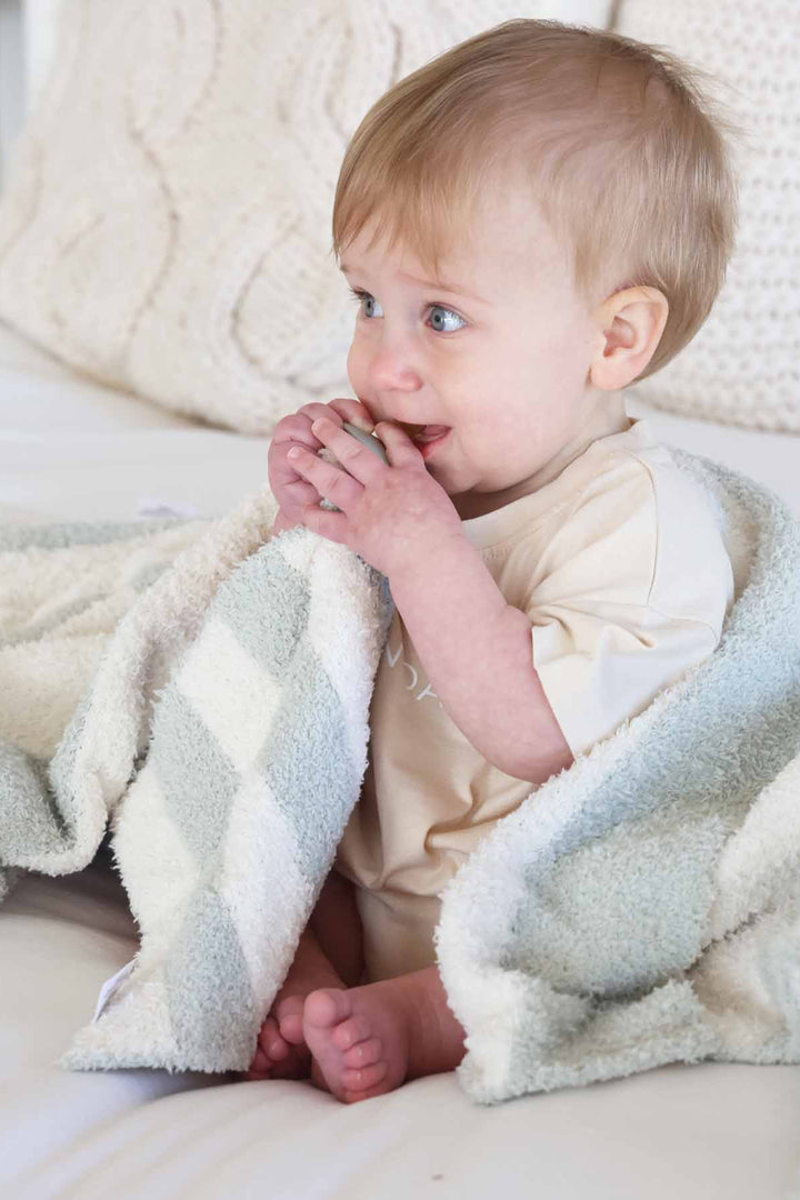 baby boy sitting on a bed holding a green and white striped plush lovey with a matching  blanket draped over him 