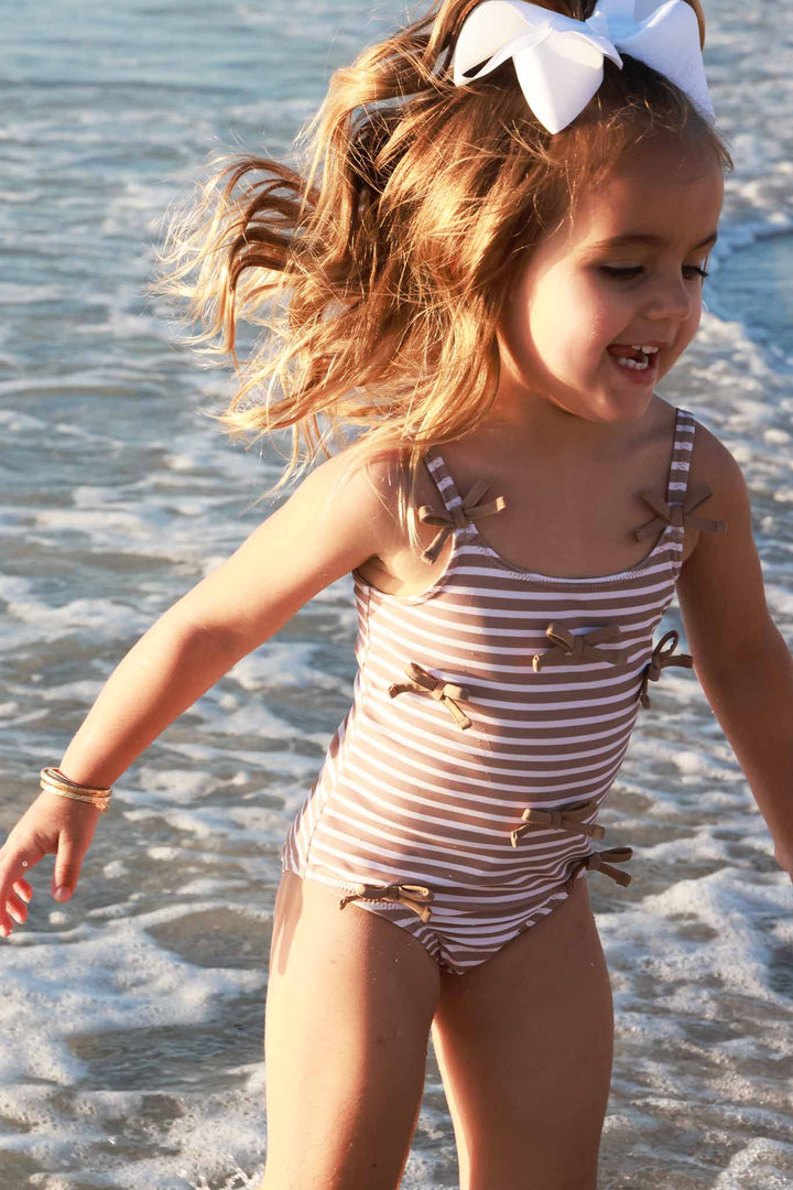 girl jumping in ocean in sandy stripes bow one piece swimsuit 