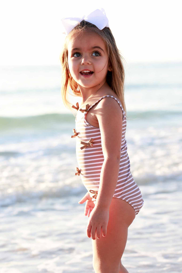 side view of girl on the beach in sandy stripe bow spaghetti strap one piece swimsuit 