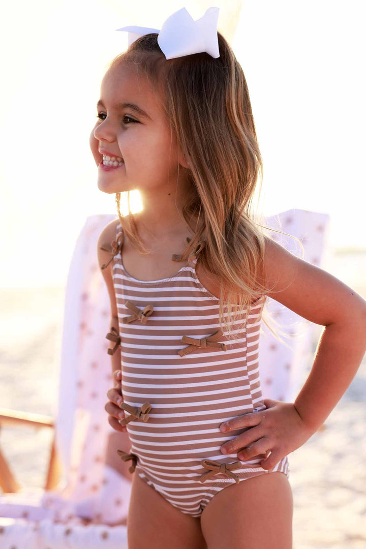 smiling girl with hands on her hips in sandy stripes bow one piece 