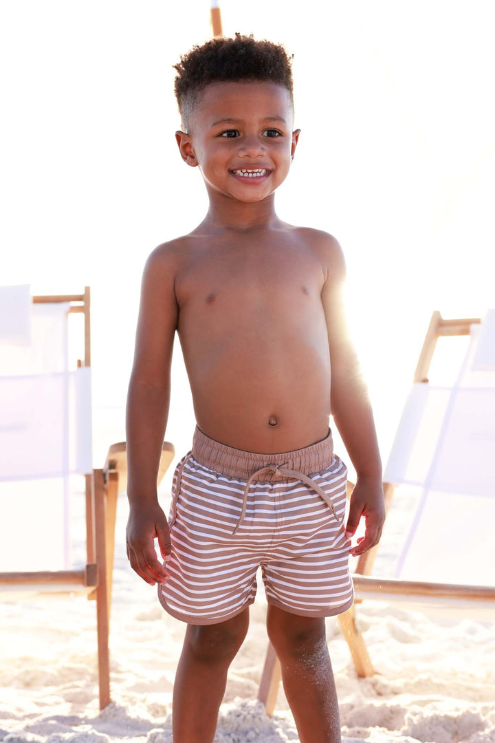 boy standing on the beach in brown and white stripe swim trunks with drawstring waist 
