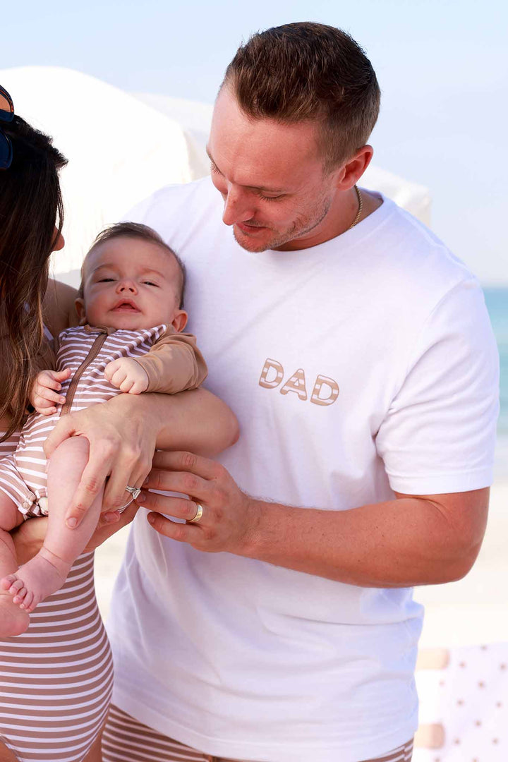 mom and dad at beach with baby wearing matching neutral stripes swimsuits 
