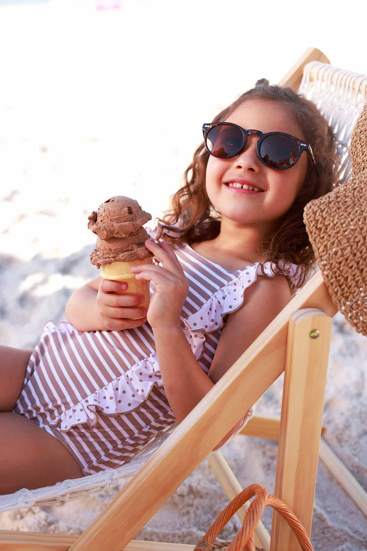 girl laying on beach chair in sandy stripes double ruffle one piece swimsuit with polka dot ruffle details 