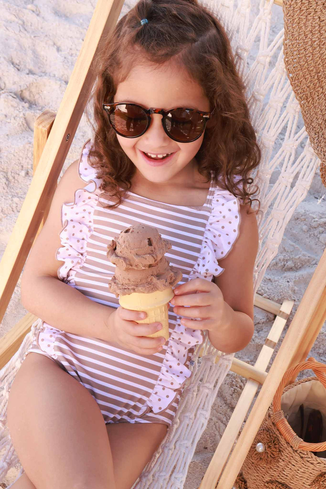 girl laying on beach chair in neutral stripe and polka dot ruffled one piece