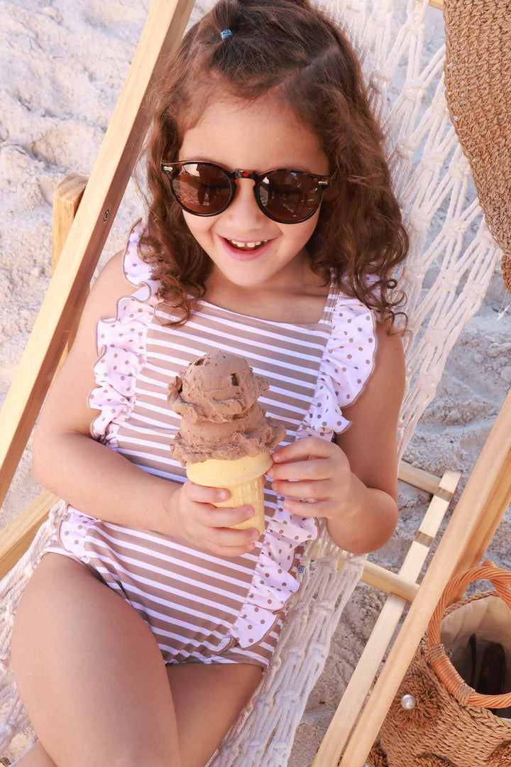girl laying on beach chair in neutral stripe and polka dot ruffled one piece