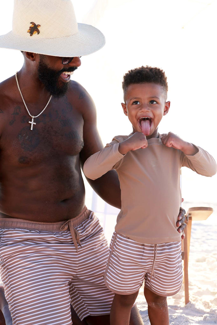 boy and son at the beach in matching stripes swim trunks with a solid brown rash guard 
