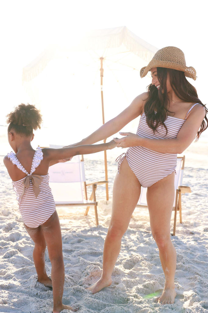 mom and daughter twirling on the beach in matching neutral stripe swimsuits 