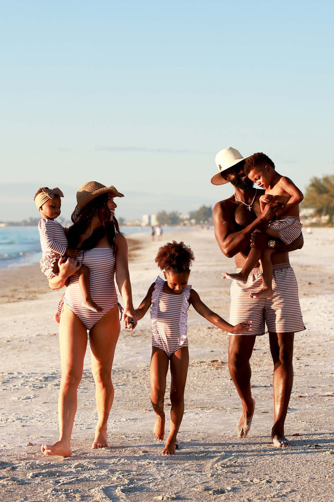 family walking on the beach in neutral stripe and polka dot matching swimsuits 