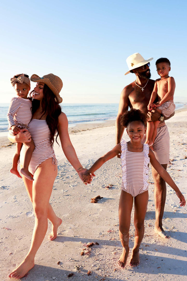 family walking on beach holding hands wearing sandy stripes matching swimsuits 