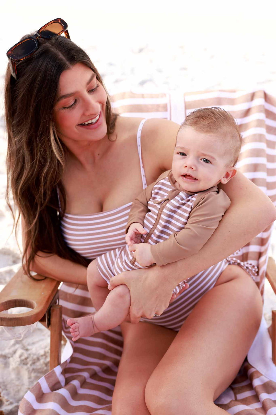mom holding baby wearing coordinating neutral stripe swimsuits 